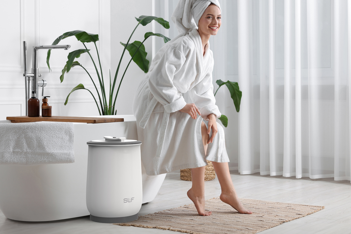 A woman in a bathroom smiling while using a warm towel from the SLF warmer.